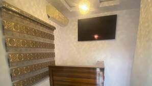A room with a patterned wall, a wooden reception desk, a flat-screen TV, and a ceiling with recessed lighting. - DE EMERITUS COURTYARD HOTEL (Abuja)