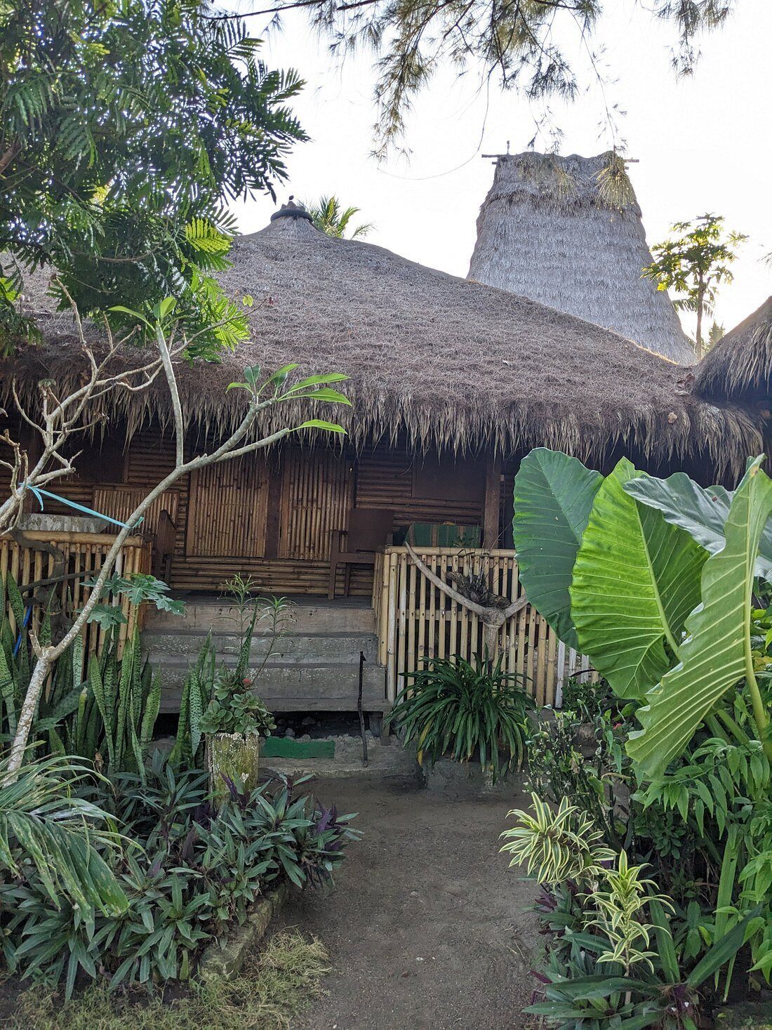 Ein traditionelles Haus mit Strohdach, einer Holzveranda und einem Feldweg davor.