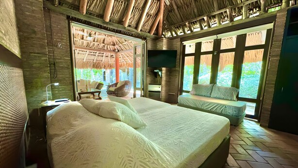 Een ruime slaapkamer met een groot bed, een zithoek, een televisie en uitzicht op groen.