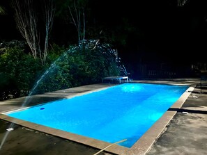 Una piscina con fuente iluminada por la noche.