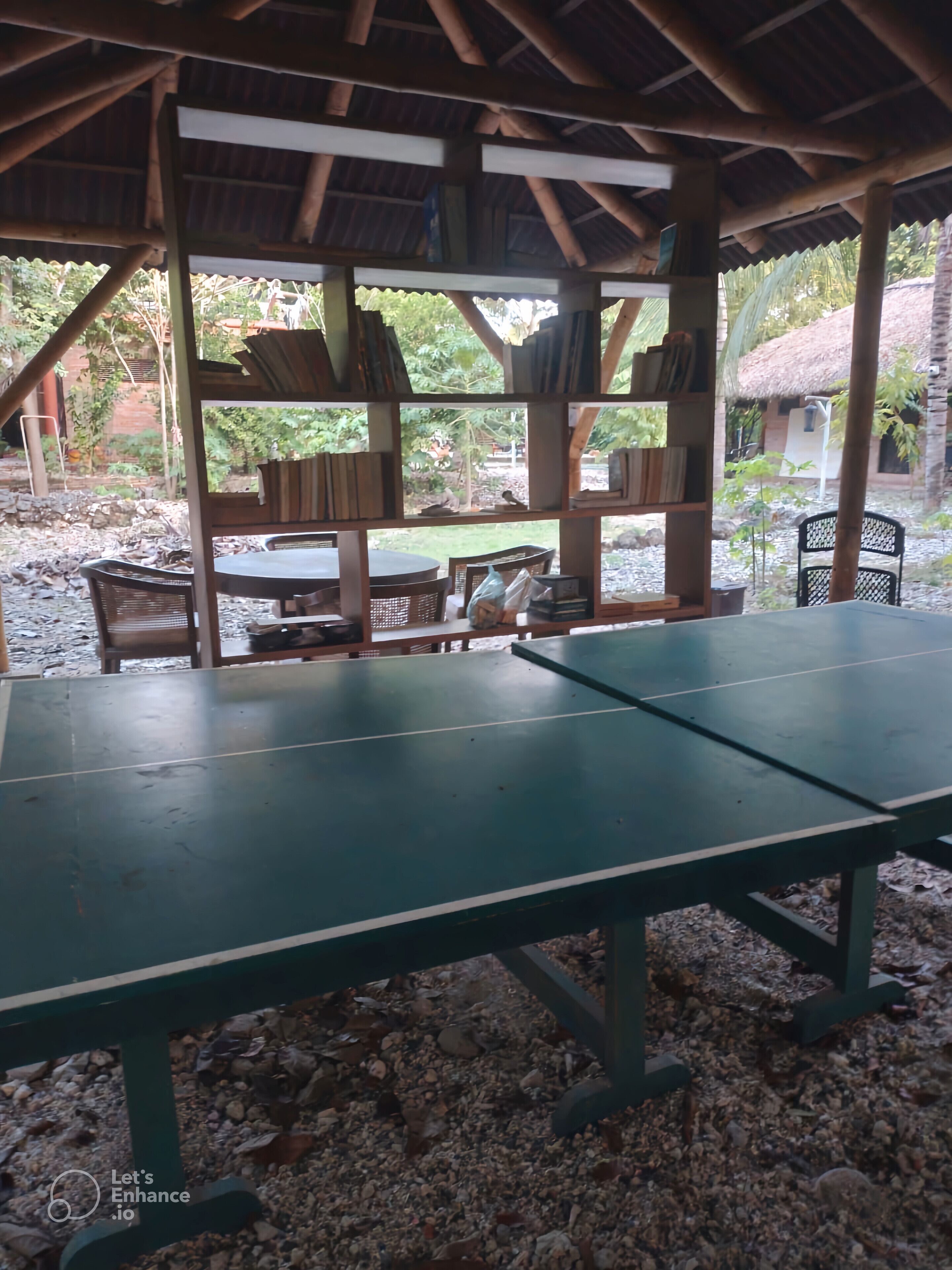 Un espacio al aire libre con mesa y sillas bajo una estructura de madera con techo de paja.