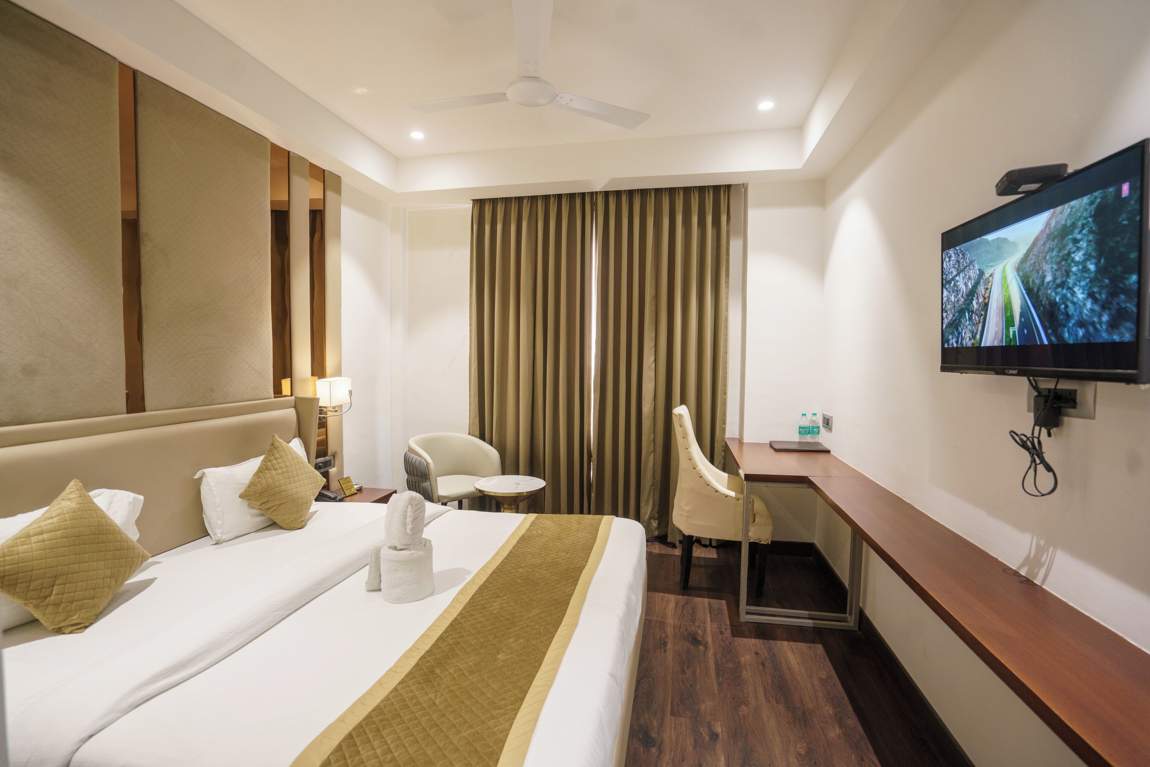 Hotelkamer met een groot bed, een bureau, een stoel, een televisie en een plafondventilator.