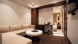 A modern hotel room with a beige sofa, a round white table, a wooden desk, and a bed with a nightstand. - Aurea by The Wallflower Hotels (Kota)