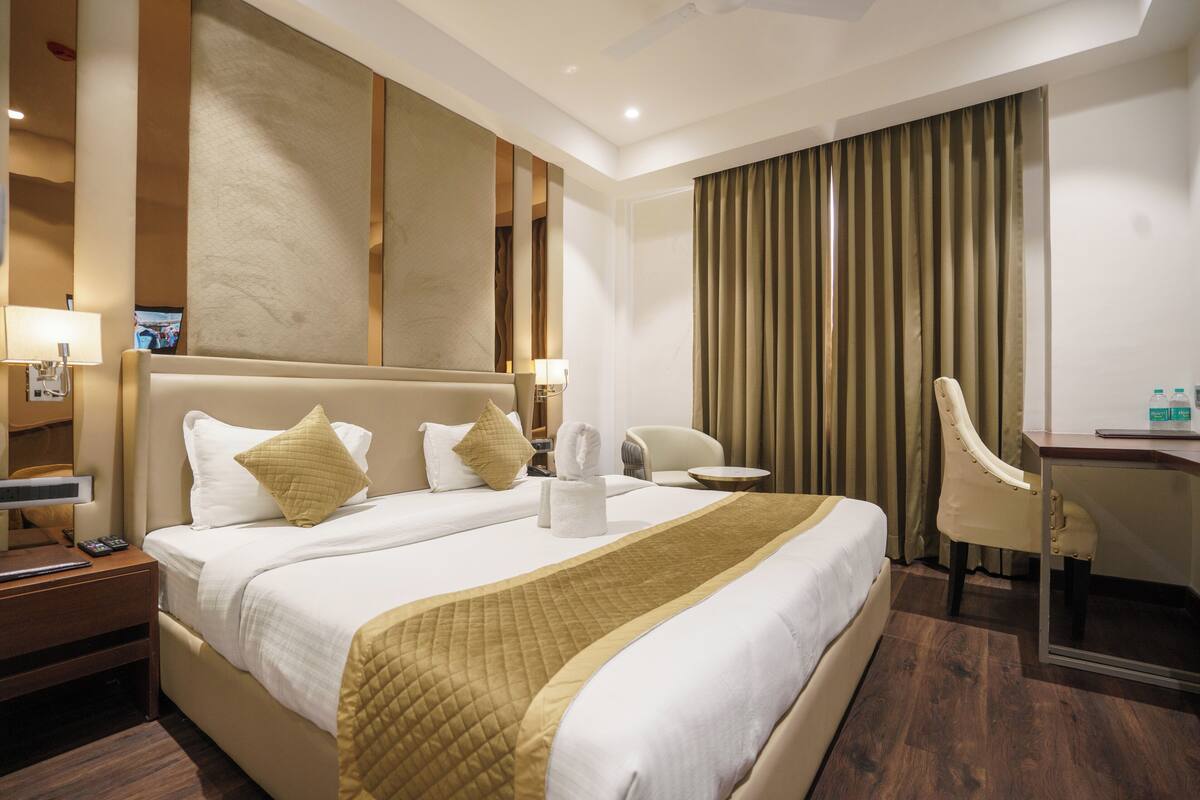 A hotel room with a large bed, a desk, a chair, and a TV.