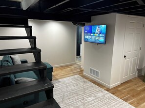 Ein Zimmer mit an der Wand befestigtem Fernseher, einer Treppe und einer Tür.