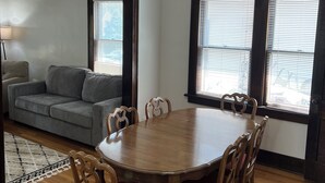 A dining area with a wooden table and chairs, a gray sofa, and a chandelier. - Cozy 4 bedroom/2 bath home in desired Benson District! (Omaha)