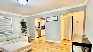 A modern living room with a sofa, a coffee table, and a pet bed. There is a kitchen in the background. - Luxurious large estate house in beautiful Alexandria! (Alexandria)