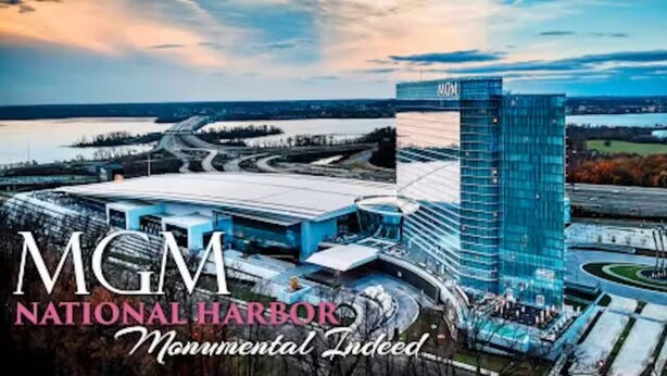 A modern building with a glass facade and a prominent 'MGM' sign, surrounded by a landscaped area and a body of water. - Luxurious large estate house in beautiful Alexandria! (Alexandria)