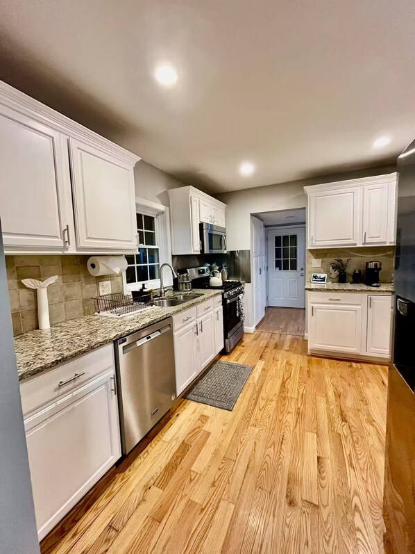 A modern kitchen with white cabinets, granite countertops, stainless steel appliances, and wooden flooring.