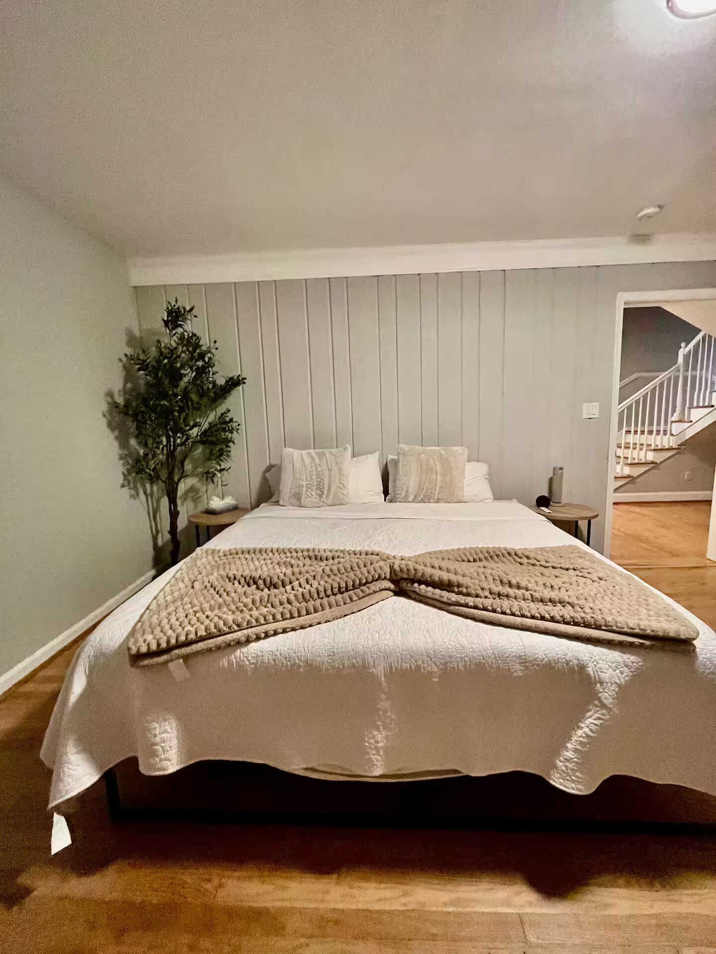 Quarto com uma cama grande, mesa de cabeceira, abajur e escada ao fundo.