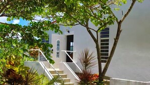 Un edificio blanco con una escalera que lleva a una puerta, rodeado de follaje.
