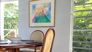 Un comedor con una mesa y sillas de madera, un cuadro enmarcado en la pared y vistas a zonas verdes a través de una ventana.