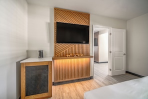 A hotel room with a wooden accent wall, a flat-screen TV mounted above a wooden console, a small coffee maker, and a bed with white bedding. - LYFE INN & SUITES by AGA- North Hollywood Universal Studios (North Hollywood)
