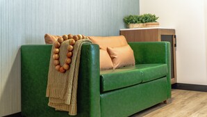 A green sofa with a beige throw blanket and wooden beads, positioned against a wall with vertical lines.