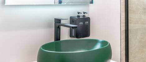 A green ceramic sink with a modern faucet on a white countertop, a soap dispenser, and a wooden cabinet below.