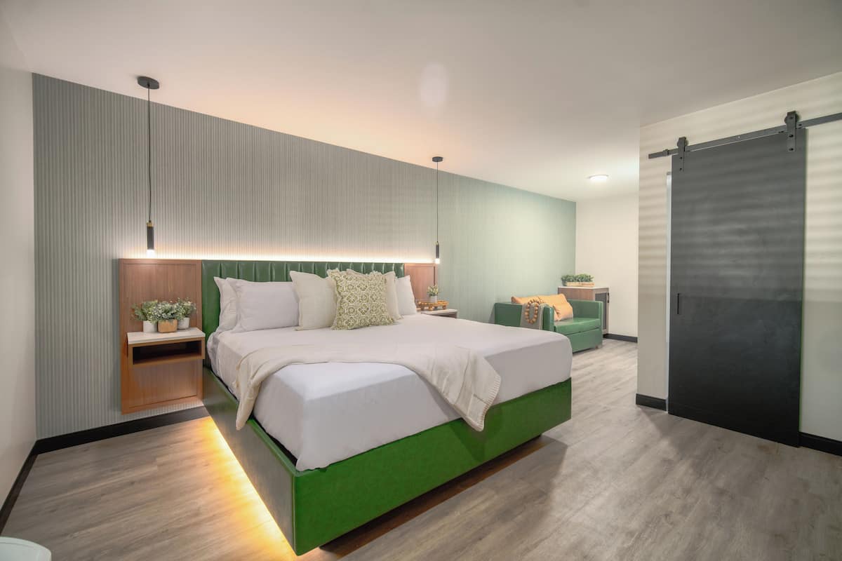 Une chambre moderne avec un lit vert, une table de chevet en bois, une chaise verte et une porte coulissante.