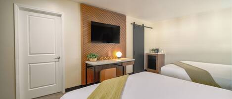 Habitación de hotel con dos camas, un escritorio con televisor, una puerta y un televisor montado en la pared.
