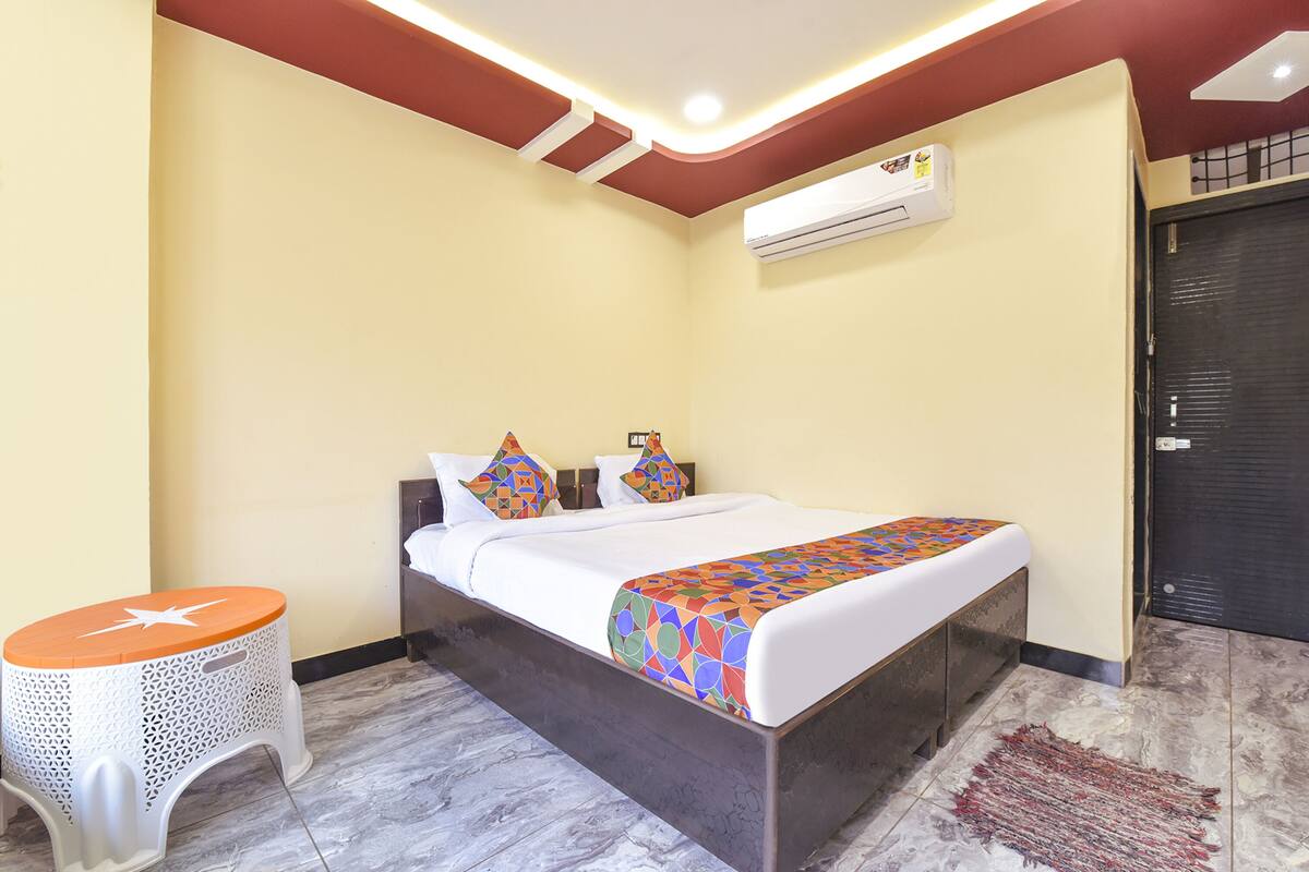 A bedroom with a bed, a small white stool, an air conditioning unit, and a door.