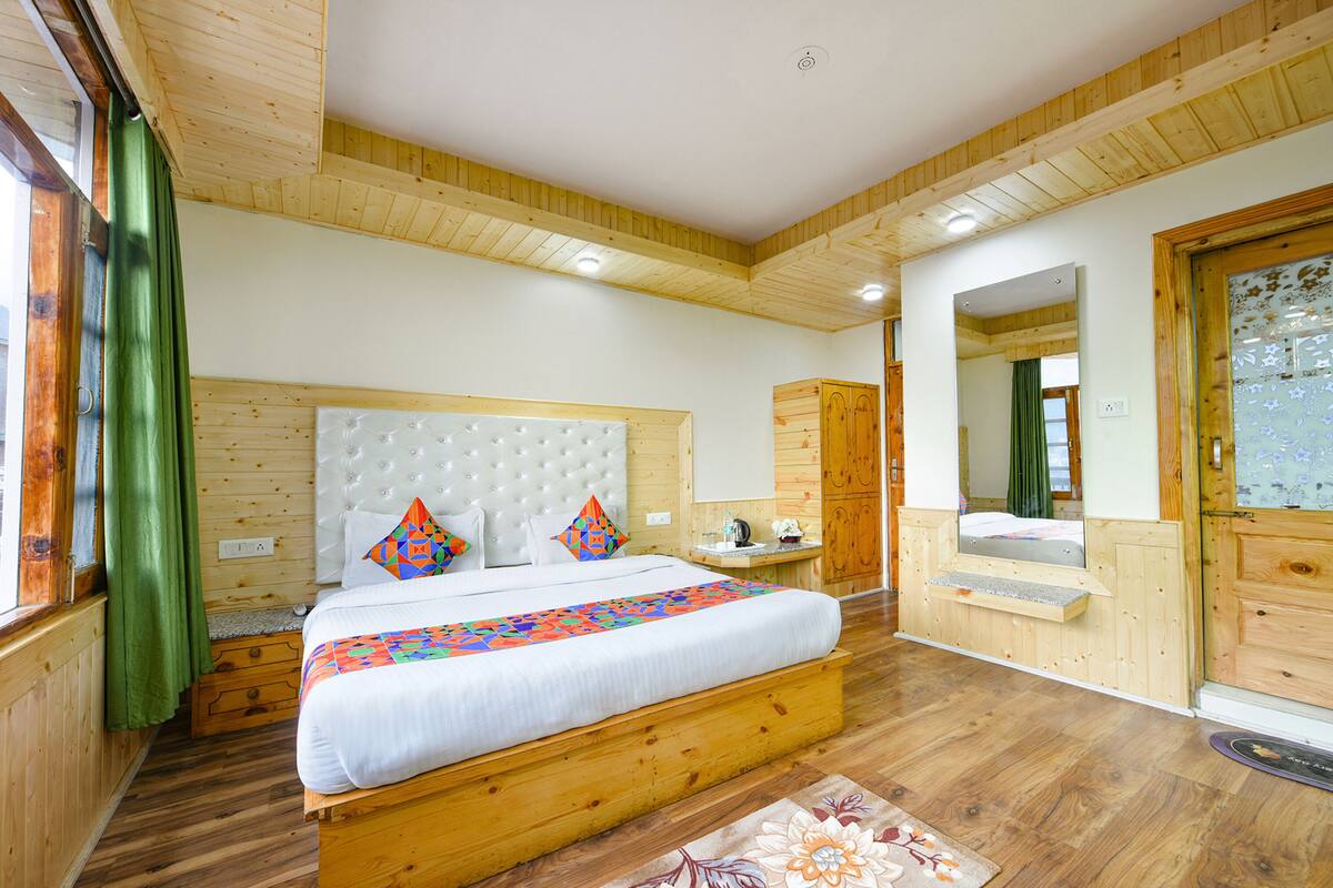 A wooden bedroom with a large bed, a nightstand, a dresser, and a mirror.