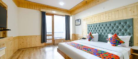 A hotel room with a large bed, wooden paneling, a view through a sliding door, and a patterned rug.