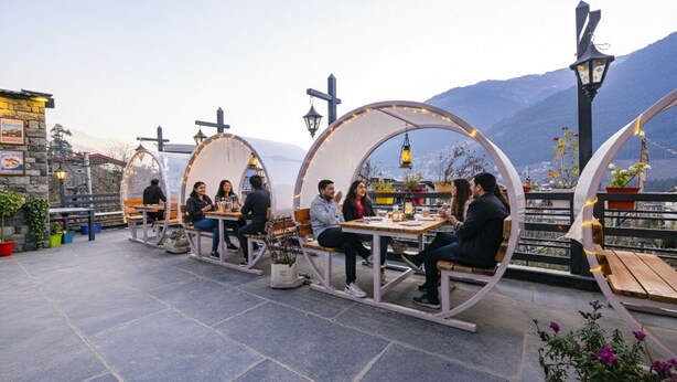 Eine Terrasse mit runden Tischen und Bänken, umgeben von Steinmauern und Topfpflanzen.