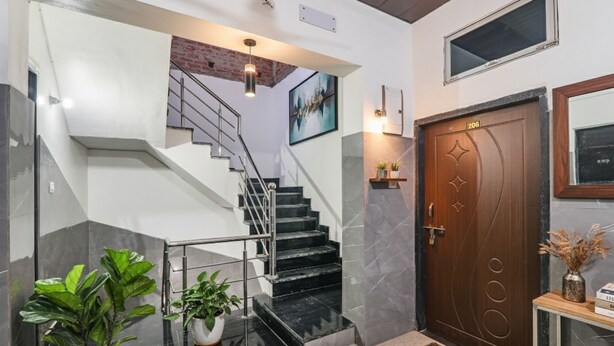 A modern interior with a staircase, a wooden door, and potted plants. - Fabexpress Milan Palace (Faizabad)