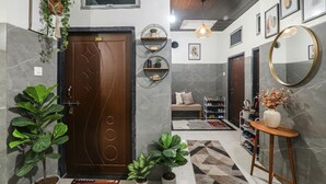 A modern hallway with a wooden door, potted plants, a mirror, and a shoe rack. - Fabexpress Milan Palace (Faizabad)