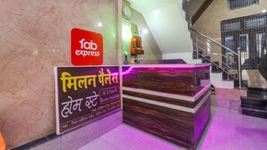 A hotel reception area with a marble wall, a reception desk, and a staircase. - Fabexpress Milan Palace (Faizabad)