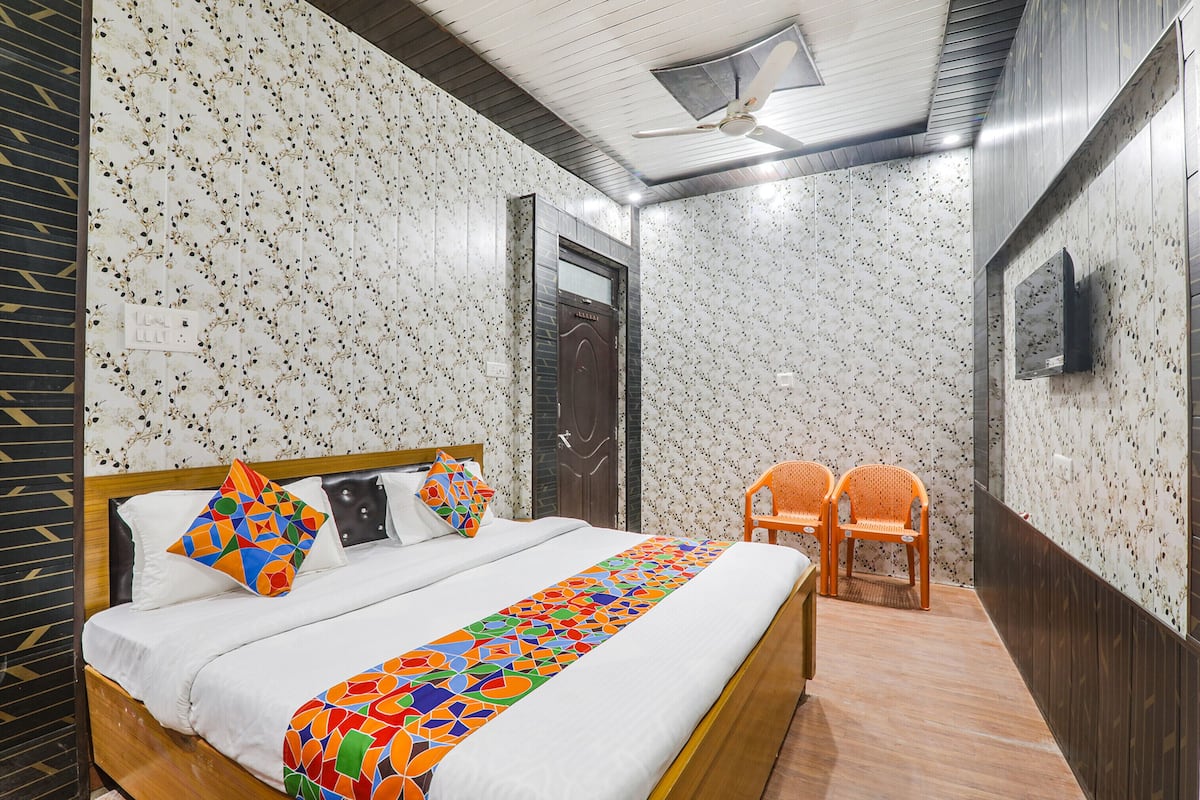 Una habitación de hotel con cama, dos sillones, televisión y ventilador de techo.