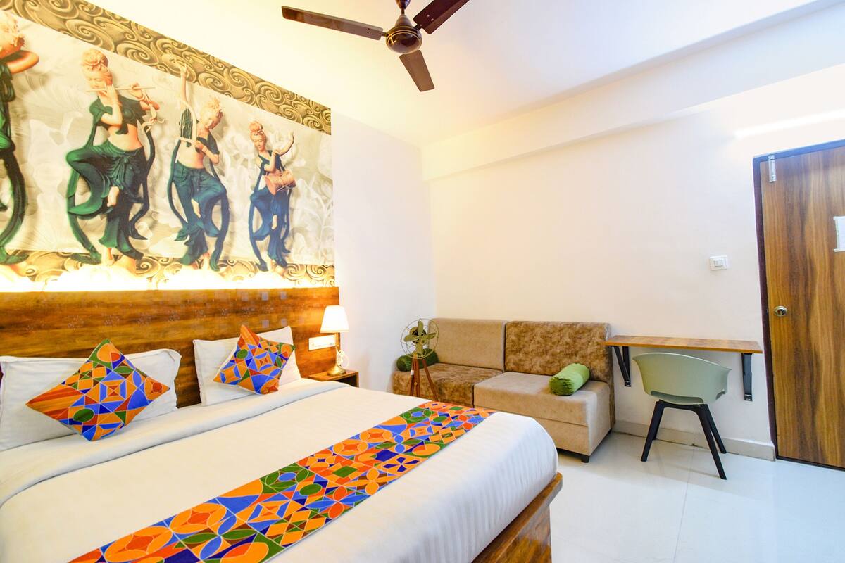 A hotel room with a large bed, a desk, a sofa, and a ceiling fan.