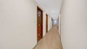 A long, narrow hallway with wooden doors on one side and a plain wall on the other. - FabHotel Hitek N - Nr. Sindhu Hospital and HITEX EXHIBITION CENTER, Hitech City (Hyderabad)
