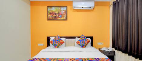 A hotel room with a bed, an air conditioner, a painting, and a curtain.