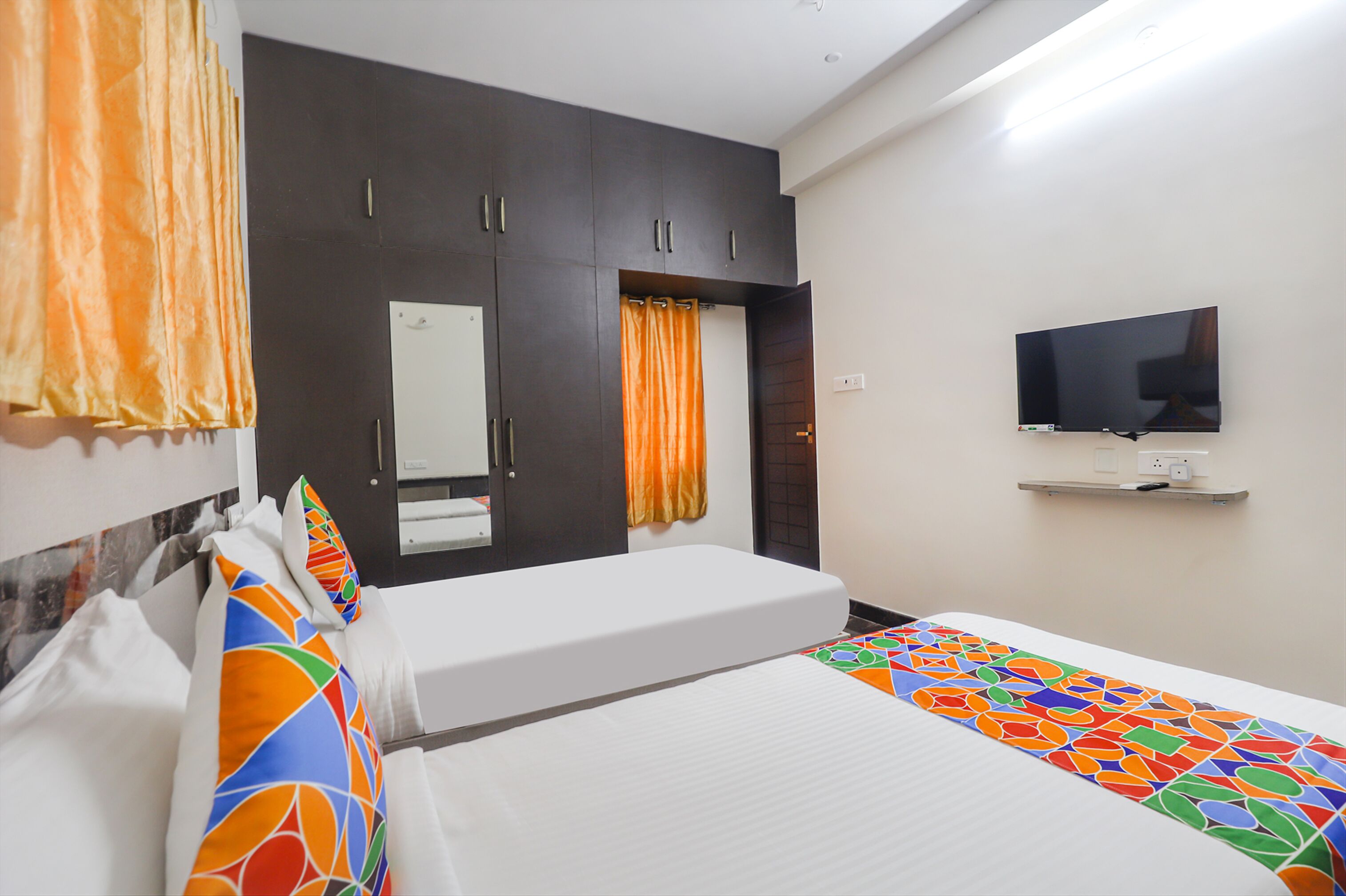 A hotel room with a bed, a TV mounted on the wall, and a wardrobe with a mirror.