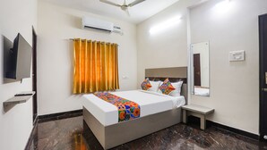 Une chambre d’hôtel équipée d’un lit, d’une télévision, d’un climatiseur, d’un ventilateur de plafond, d’un miroir et d’une petite table de chevet.