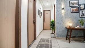 A hallway with wooden doors, a potted plant, a table with a lamp, and framed pictures on the wall. - FabHotel Prime Jashan Paradise - MP Nagar (Bhopal)