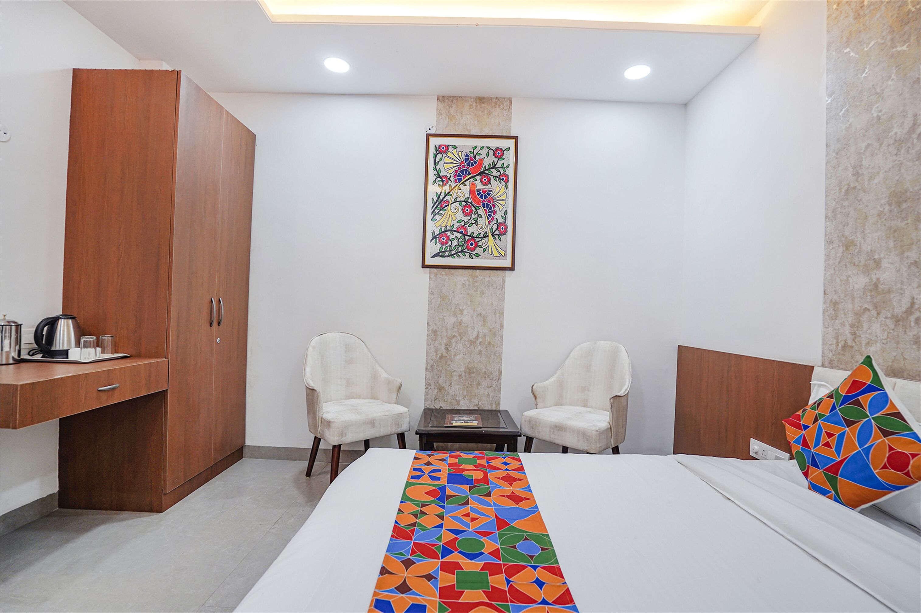 A hotel room with a bed, a desk, two chairs, a coffee maker, and a painting on the wall.