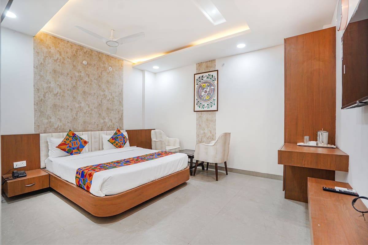 A modern hotel room with a large bed, a desk, a chair, and a TV.