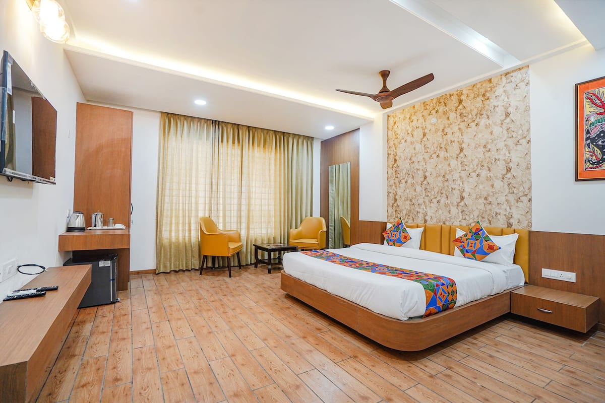 A hotel room with a bed, two chairs, a desk, a TV, and a ceiling fan.