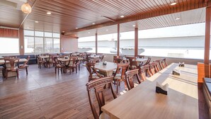 A spacious dining area with wooden tables and chairs, large windows, and a view of the sea. - FabHotel Prime Jashan Paradise - MP Nagar (Bhopal)