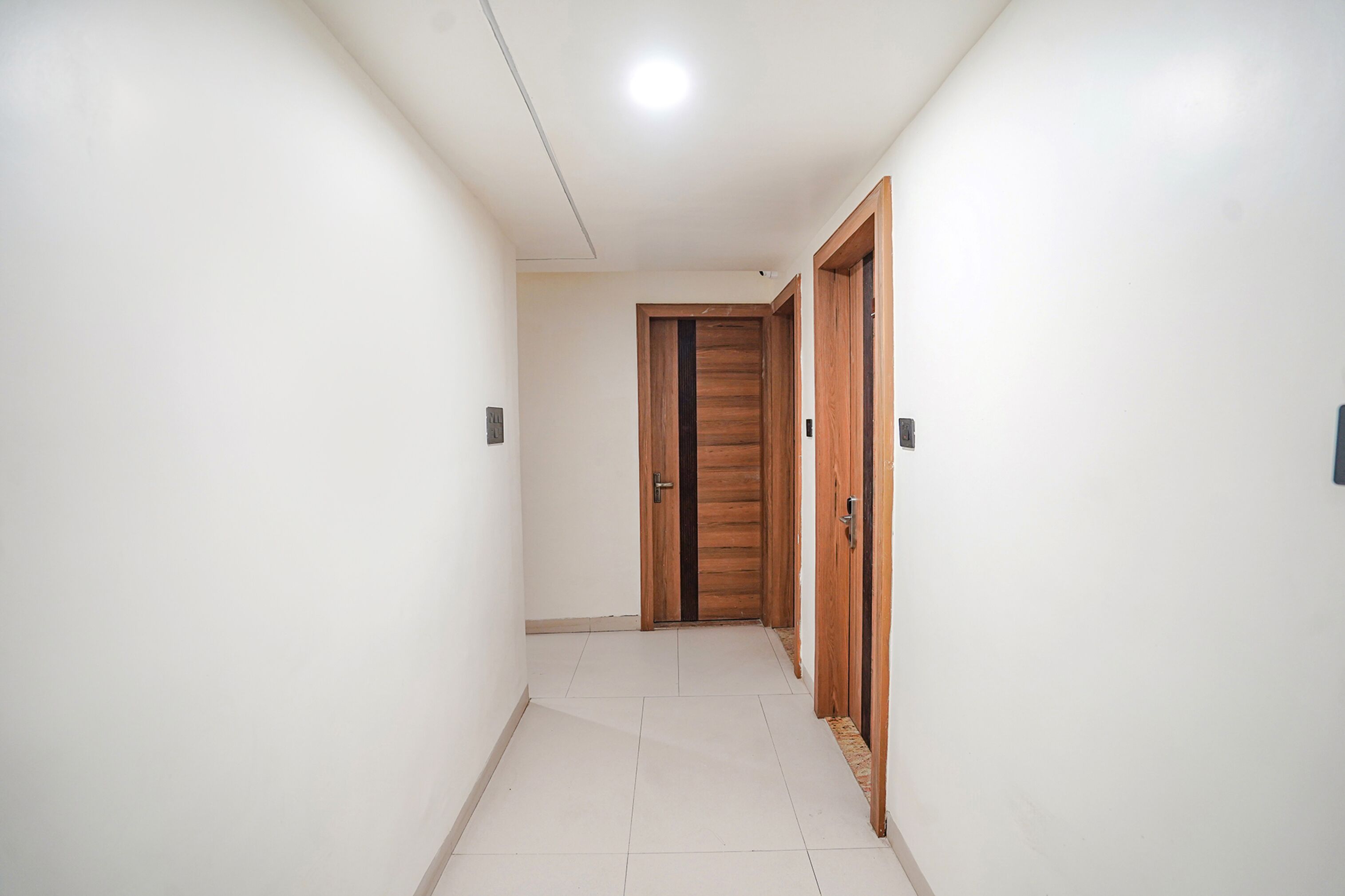 Un corridoio con pareti bianche, pavimento piastrellato e porte in legno.