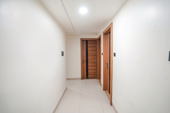 Un pasillo con paredes blancas, piso de baldosas y puertas de madera.