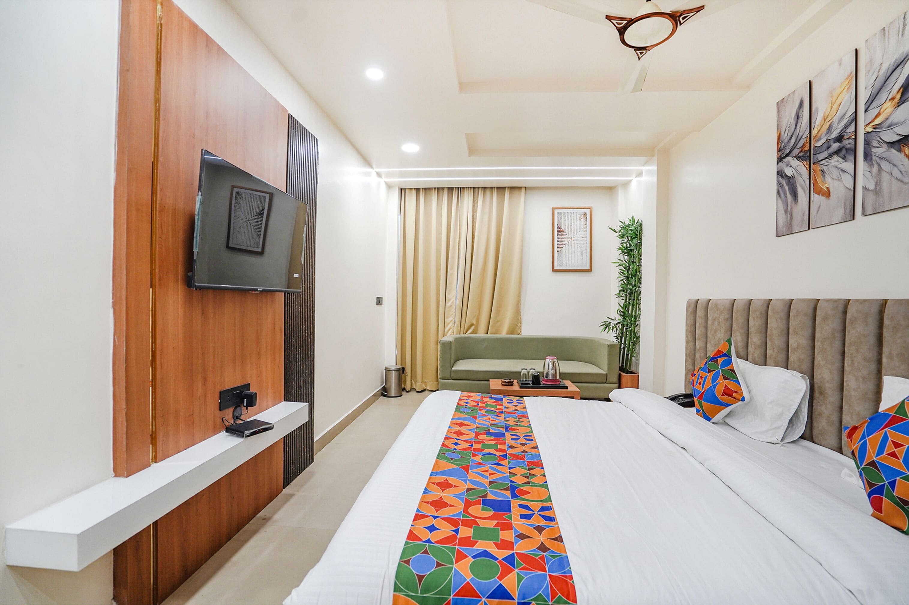 Una habitación de hotel moderna con una cama grande, un televisor montado en un panel de madera, un sofá verde y un ventilador de techo.