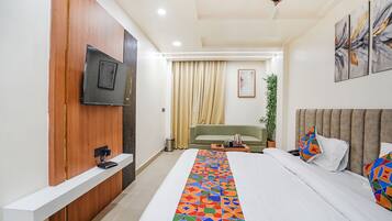 Una habitación de hotel moderna con una cama grande, un televisor montado en un panel de madera, un sofá verde y un ventilador de techo.