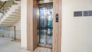 Un ascenseur moderne doté d’une structure en bois et de portes en verre, situé dans un immeuble qui possède un escalier et une rambarde en verre.