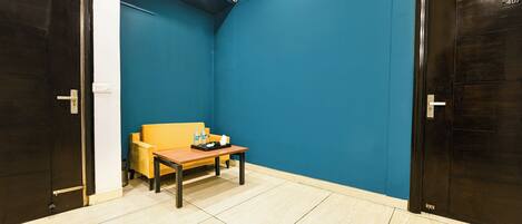 Una habitación pequeña con una pared azul, un sofá amarillo, una mesa de madera con una bandeja de objetos y dos puertas de madera oscura.