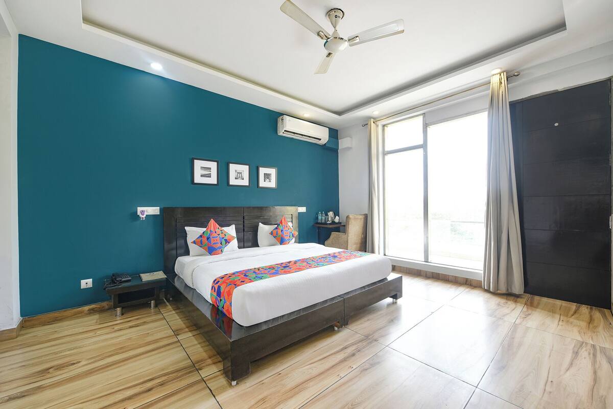 Une chambre d’hôtel moderne avec un grand lit, un ventilateur de plafond, une fenêtre avec des rideaux et un plancher en bois.