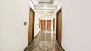 A hallway with wooden doors, a marble floor, and recessed lighting. - Fabhotel Vibe (Noida)