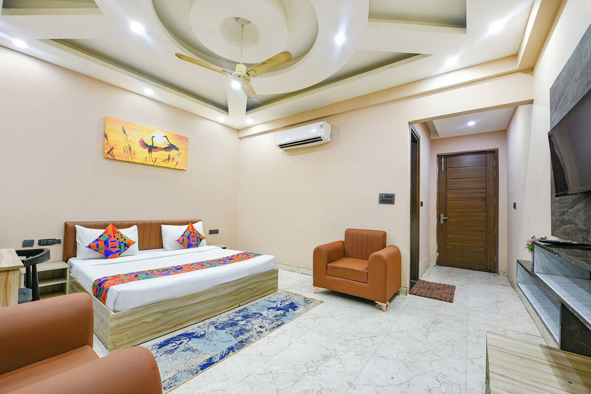A hotel room with a bed, a chair, a TV, and an air conditioning unit.