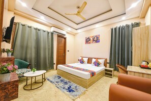 A hotel room with a bed, a round table, a chair, a small stool, a potted plant, and a ceiling fan. - Fabhotel Vibe (Noida)