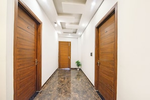 A hallway with wooden doors, a potted plant, and a marble floor. - Fabhotel Vibe (Noida)